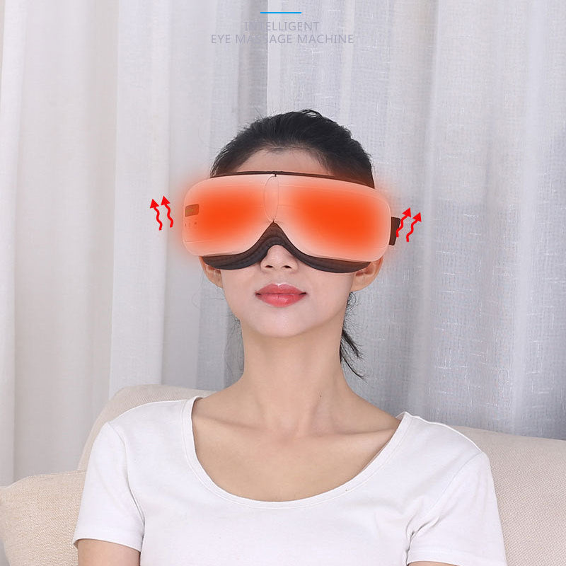 A woman wearing a red eye massager and a white t-shirt sitting on a beige sofa in front of white curtains.
